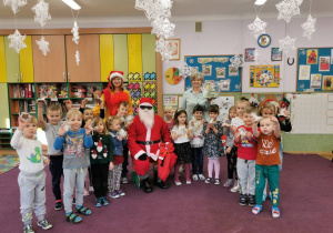 Dzieci stoją z Mikołajem i trzymają w rękach słodycze.